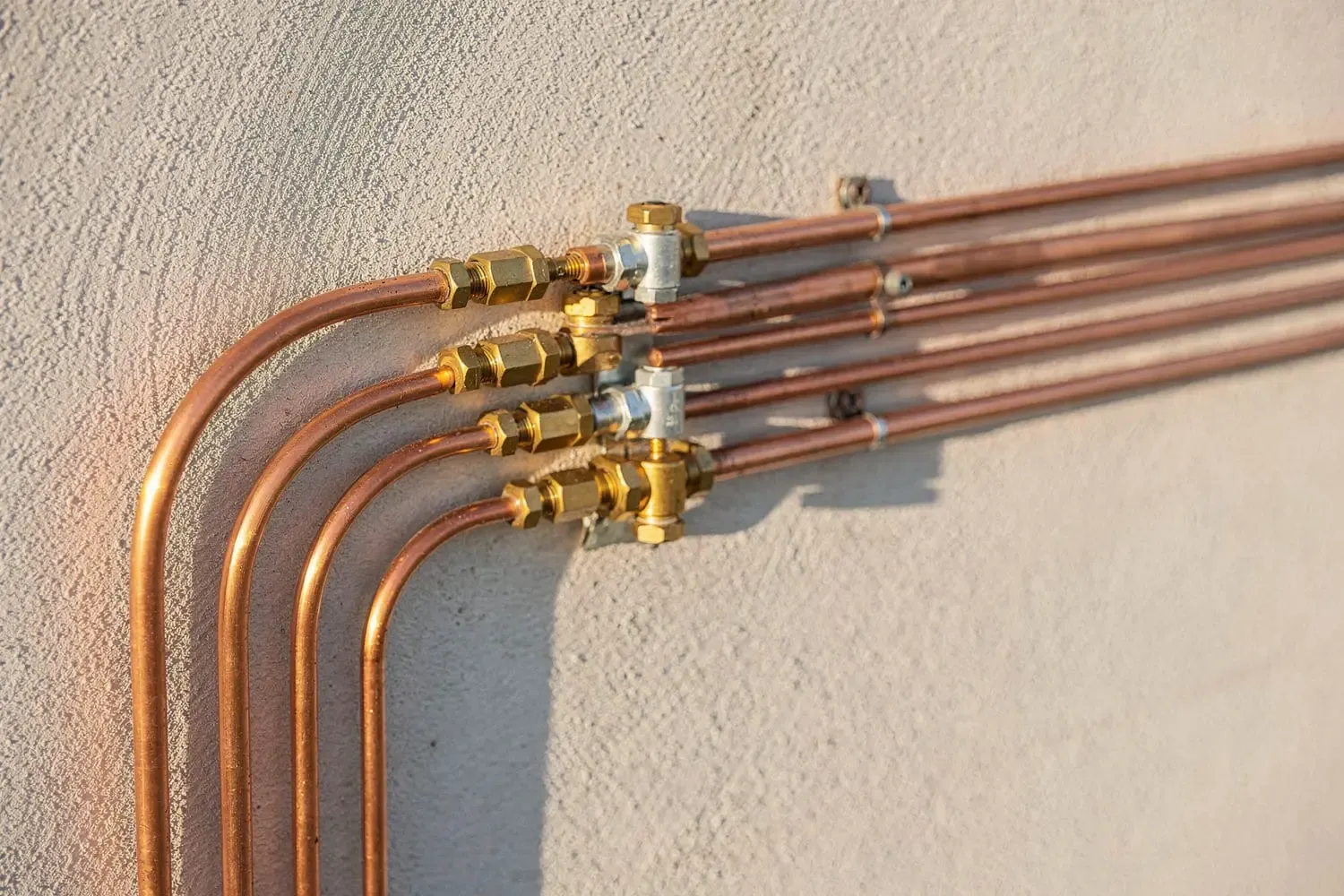Copper refrigerant lines and brass fittings running along a wall in warm Colorado light — precise, skilled work